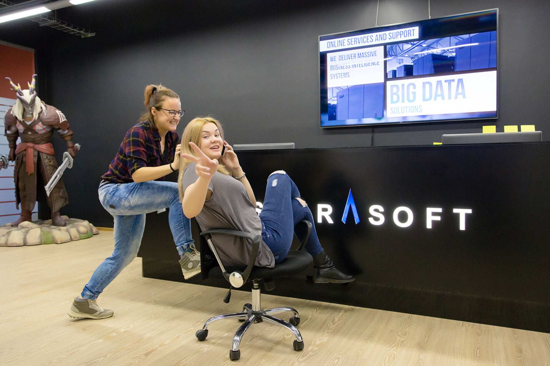 A woman pushing another on an office chair